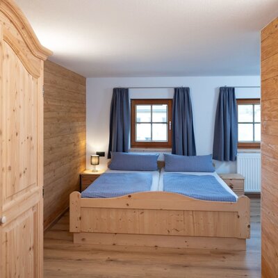 Camera da letto nell'Ap­par­te­ments con letto matrimoniale in legno, armadio in legno e due finestre.
