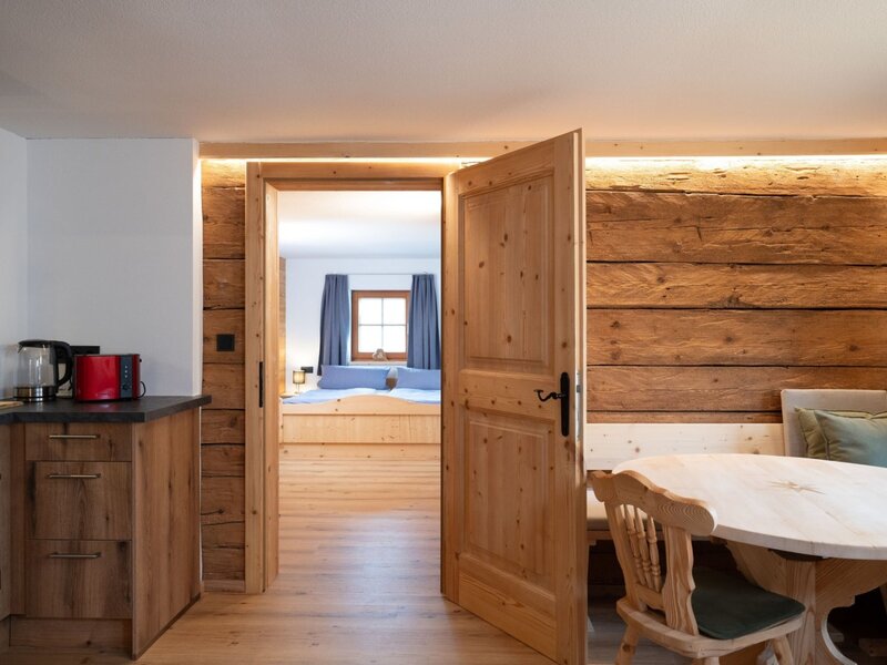 Zona cucina e pranzo dell'Ap­par­te­ments, con arredi in legno e accesso a una camera da letto.