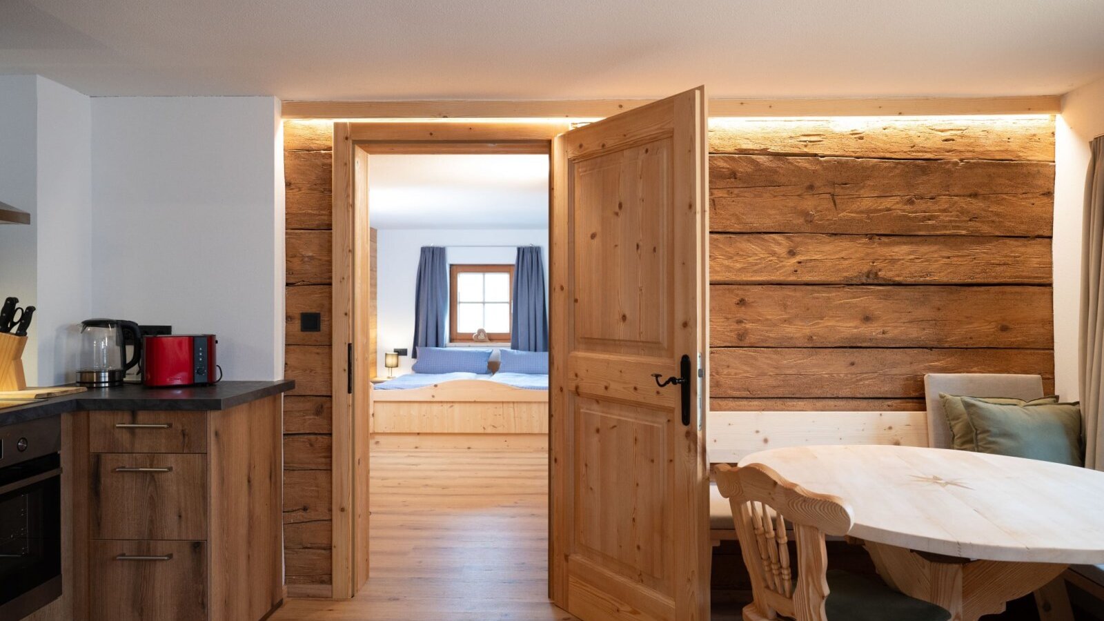 Zona cucina e pranzo dell'Ap­par­te­ments, con arredi in legno e accesso a una camera da letto.