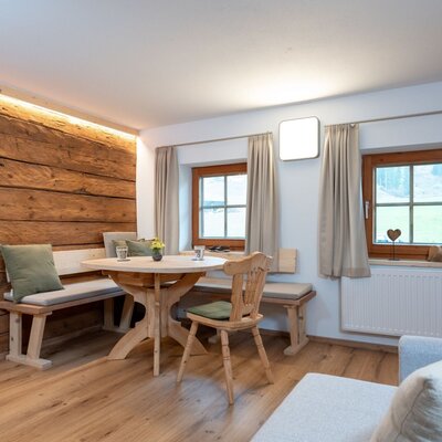 Zona giorno e pranzo dell'appartamento con tavolo in legno, panca ad angolo e due finestre.