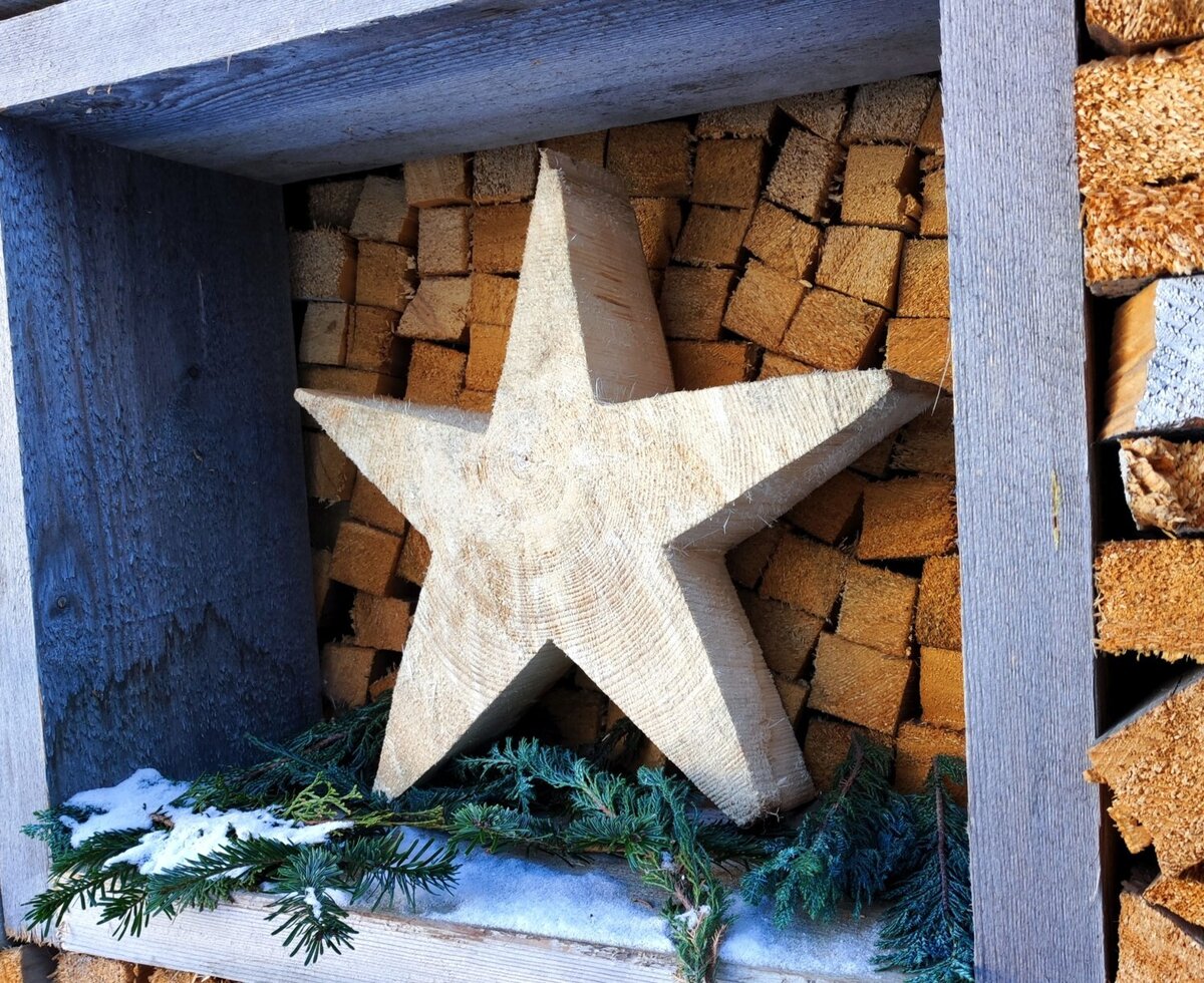 Stella di legno decorativa nella catasta di legna del maso, con rami di abete e neve.