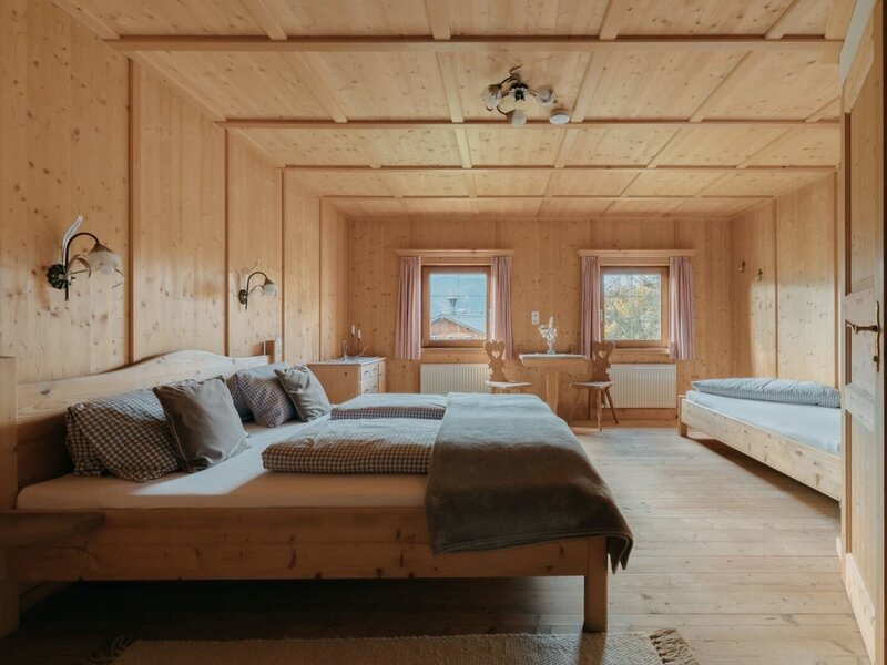 Camera da letto della Ferienwohnung con letto matrimoniale, letto singolo, rivestimento in legno e un tavolino con sedie.