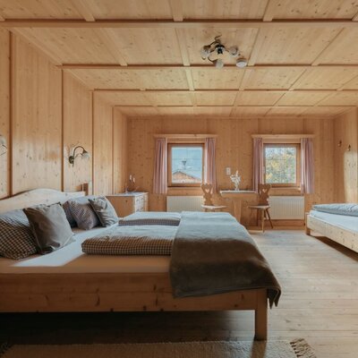 Camera da letto della Ferienwohnung con letto matrimoniale, letto singolo, rivestimento in legno e un tavolino con sedie.