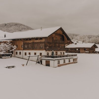 La Ferienwohnung coperta di neve con facciata in legno, una terrazza e un parco giochi, immersa in un paesaggio invernale.