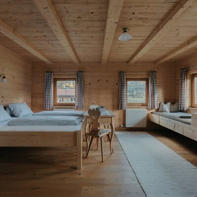 Camera da letto nell'appartamento vacanze con pareti in legno, due letti singoli e una panca in legno come posto letto aggiuntivo.