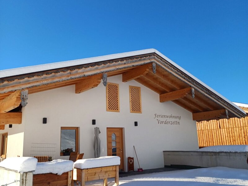 L'esterno invernale dell'agriturismo 'Ferienwohnung Vorderzettla', coperto di neve sotto un cielo azzurro.