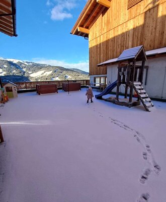 L'area esterna innevata del Bauernhof, con parco giochi per bambini e vista sulle montagne.