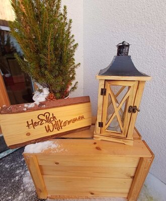 Un invitante benvenuto all'ingresso dell'agriturismo con un'insegna rustica in legno, una lanterna e decorazioni invernali.